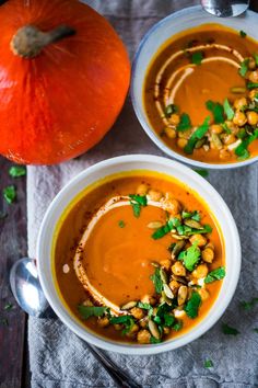 two white bowls filled with soup next to an orange pumpkin