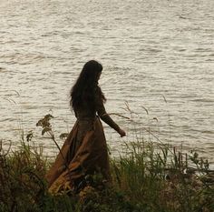 a woman in a long dress walking by the water