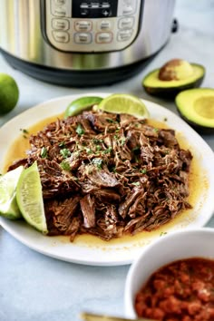 a white plate topped with shredded beef and garnished with limes next to an instant pot roast