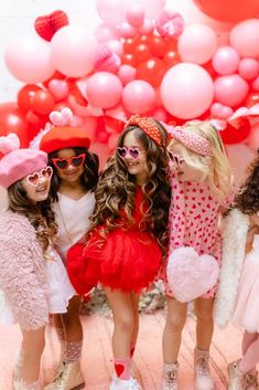 three girls dressed up in costumes standing next to each other with pink balloons behind them