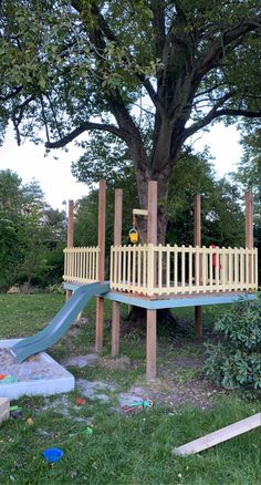 a wooden play set in the middle of a park with a slide and climbing frame