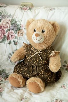 a brown teddy bear sitting on top of a bed next to a flower covered pillow