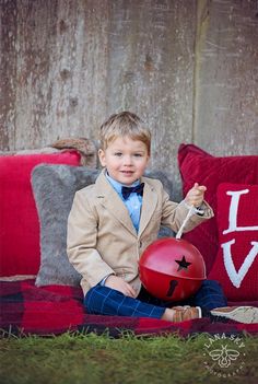 a young boy in a suit and bow tie sitting on a couch holding a red ball