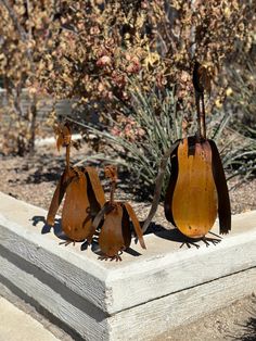 three metal birds sitting on top of a cement block in front of a planter