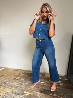 Rock a relaxed look in this dreamy denim duo! Boastin' a rapel collar, short sleeve jacket, button close, and back belt, this blue washed denim top is totally off the hook. Meanwhile, wide leg, ankle length pants are sure to have all eyes on ya! 75.6% Cotton 15% Viscose 9.4% Polyester. Model is 5'7" and wearing a size Medium. Summer Denim Blue Flare Jeans With Button Closure, Medium Wash Denim Jumpsuit With Short Sleeve For Work, Cropped Dark Wash Denim Jacket For Summer, Casual Summer Flare Jeans With Button Closure, Workwear Cropped Denim Jeans, Spring Cropped Dark Wash Jeans, Washed Blue Button-up Jeans For Summer, Summer Washed Blue Button-up Jeans, Summer Button-up Washed Blue Jeans