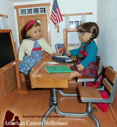 two dolls are sitting at a table in front of a blackboard with an american flag on it