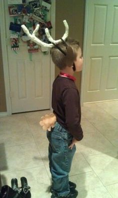 a young boy standing in front of a door wearing a reindeer antlers headband