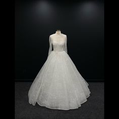 a white wedding dress on display in a dark room with black walls and flooring