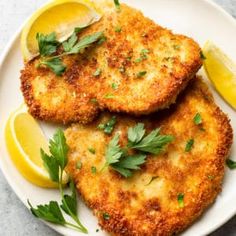 two fried fish fillets on a plate with lemons and parsley