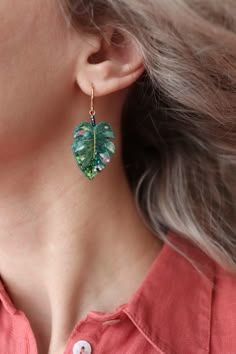 a woman wearing a pair of earrings with green leaves on it and a button in front of her ear