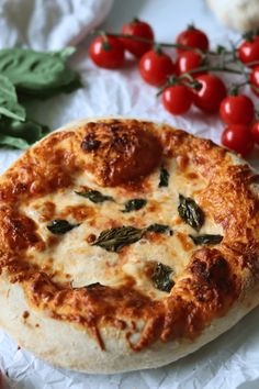 a pizza sitting on top of a piece of wax paper next to tomatoes and basil