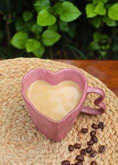 a heart shaped coffee mug sitting on top of a straw hat next to coffee beans