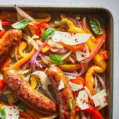 sausages, peppers, onions and cheese on a baking pan with basil sprigs