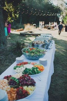 a long table filled with lots of food on top of a grass covered field next to trees