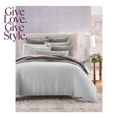 a bed with grey sheets and pillows on top of it in front of a wall