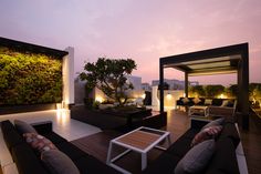 an outdoor living area with couches, tables and plants on the wall at dusk