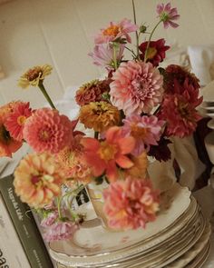 a stack of plates topped with flowers on top of a table next to a pile of books