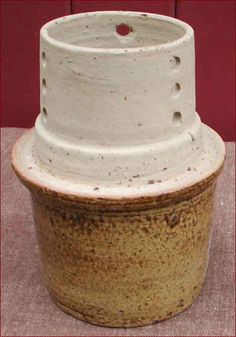 a white and brown vase sitting on top of a cloth covered table next to a red wall