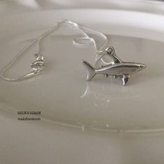 a small silver shark necklace on a white plate