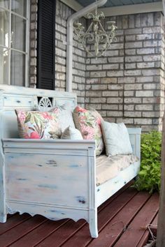 a white bench sitting on top of a wooden floor next to a brick building with a chandelier hanging from it's ceiling