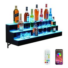 there are many bottles and glasses on the shelf with remotes next to it,