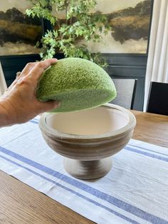 a person is holding a green sponge over a bowl