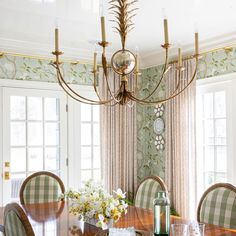 a chandelier hangs over a dining room table with chairs and vases on it