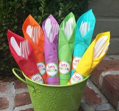 a green bucket filled with lots of different colored utensils and paper napkins