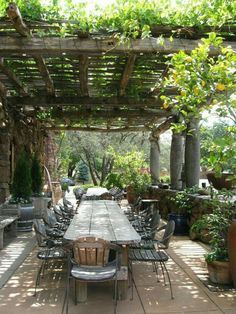 an outdoor dining area with tables and chairs under a pergolated roof, surrounded by potted plants