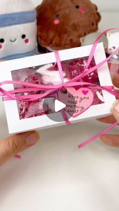 someone is holding up a small box with hearts in it and two cupcakes on the other side