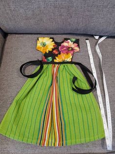 a green striped dress with flowers on the back and white ribbon around the waist, sitting on a gray couch