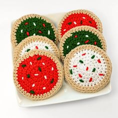 four crocheted coasters on a white plate with red, green and white designs