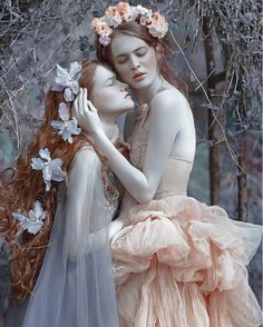 two women in dresses hugging each other with flowers on their head and hands behind them