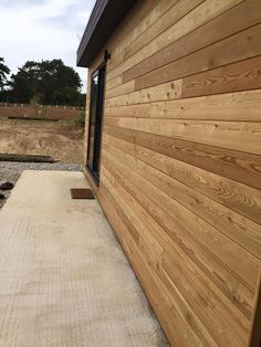 the side of a house with wood siding on it's sides and gravel in front