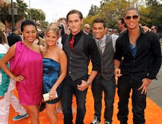 a group of people standing next to each other on a orange carpet at an event