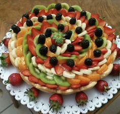 a fruit pizza on a white doily with strawberries, oranges and blackberries