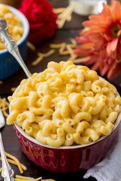 a bowl filled with macaroni and cheese on top of a table next to flowers