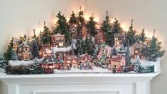 a fireplace mantel decorated with christmas trees and lit up houses in the snow at night