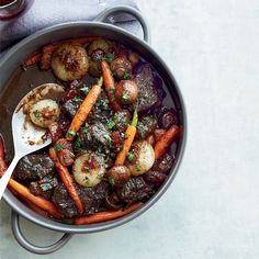 a pot filled with meat, potatoes and carrots on top of a white table