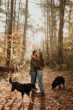 an engaged couple cuddles in the woods with their dogs as they stand next to each other