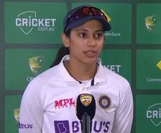 a woman standing in front of a microphone and wearing a white shirt with purple letters on it