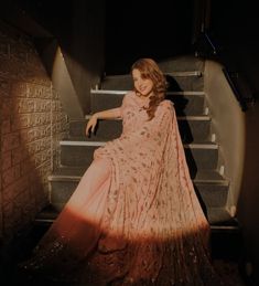 a woman is sitting on the stairs in a pink and gold dress with her hand on her hip