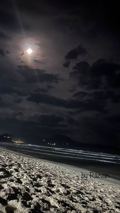 a full moon is seen over the ocean on a cloudy night at the beach with footprints in the sand