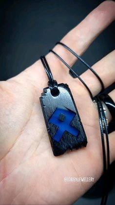 a person's hand holding a black and blue pendant with a cross on it