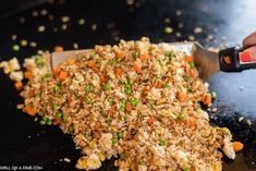 someone using a knife to cut up food on top of a black surface with peas and carrots