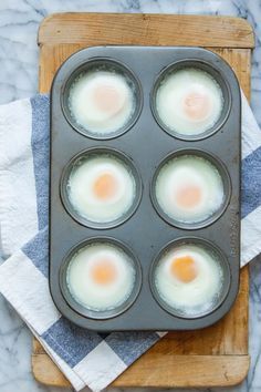 four eggs in a muffin tin on top of a cutting board with napkins