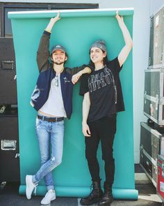 two people standing next to each other in front of a large blue wall with their arms up