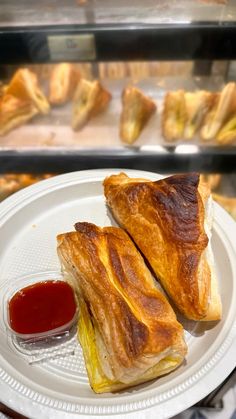 two croissants sitting on top of a white plate next to ketchup