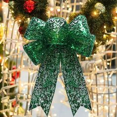 a green bow hanging from the side of a christmas wreath with lights in the background