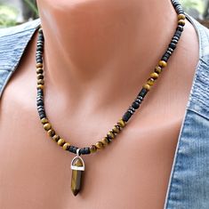 Unleash the captivating energy of this Tiger Eye Point Pendant Beaded Necklace, a stunning piece of boho stone jewelry. The focal point is a mesmerizing Tiger Eye Point Pendant, surrounded by a harmonious blend of 6mm round Tiger Eye and Matte Onyx beads. The rich, earthy tones extend to the black coconut wood beads, while hematite accent beads add a touch of sophistication. Crafted with precision using steel wire and a secure clasp, this necklace seamlessly combines style and durability for a u Black Bohemian Beaded Gemstone Necklace, Black Bohemian Crystal Gemstone Necklaces, Black Bohemian Crystal Necklace With Gemstone, Black Bohemian Crystal Gemstone Necklace, Bohemian Onyx Gemstone Beads Jewelry, Bohemian Onyx Jewelry With Gemstone Beads, Bohemian Onyx Gemstone Beaded Jewelry, Bohemian Handmade Hematite Jewelry, Handmade Bohemian Onyx Beaded Necklace